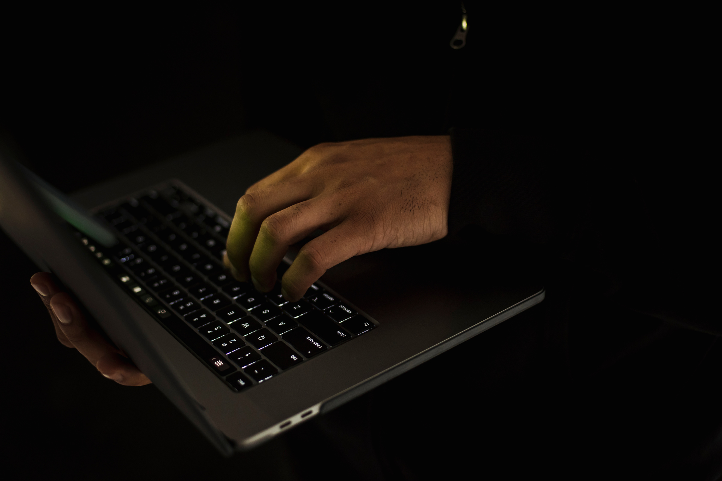 Crop faceless man typing on laptop keyboard in darkness